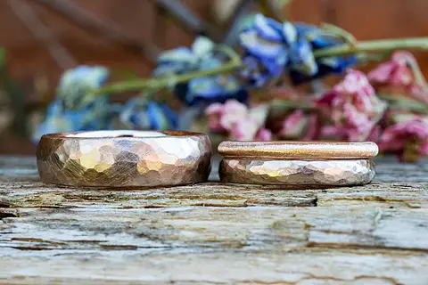 Eheringe aus Rosépalladium. Der linke Ring ist breit und hat eine gehämmerte Oberfläche. Der rechte Ring ist schmal mit Hammerschlag und ist mit einem schlichten Vorsteckring kombiniert.