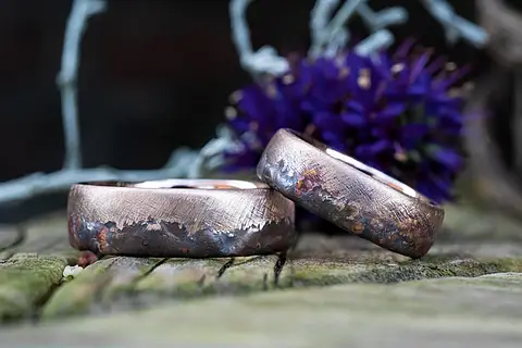 Besondere Eheringe aus Rotgold mit einer individuell gestalteten Oberfläche aus matten und angeflemmten Bereichen. Eheringe mit rustikaler Struktur