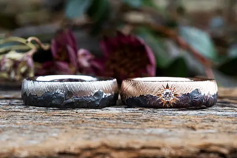 Besondere Eheringe aus Rotgold mit einer schwarzen liquid Oberfläche und einem Diamanten in Polarstern Optik