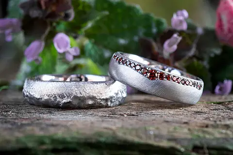 Ausgefallene Eheringe aus Weißgold und Platin. Der Herrenring hat eine auffällige Oberfläche und der Damenring ist mit roten Brillanten bestückt